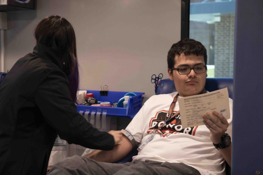 Junior Gustavo Tejada reads his donor card as the nurse preps him for donation. 